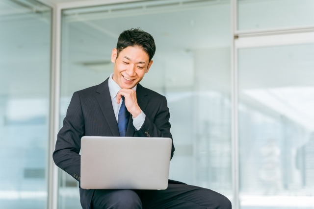 イメージ写真：パソコンののぞき込みながら、笑顔を見せている男性のビジネスパーソン