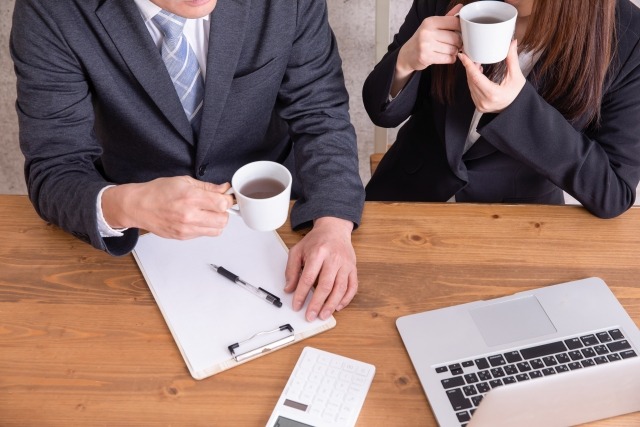 イメージ写真：コーヒーを飲みながら話している男女のビジネスパーソン
