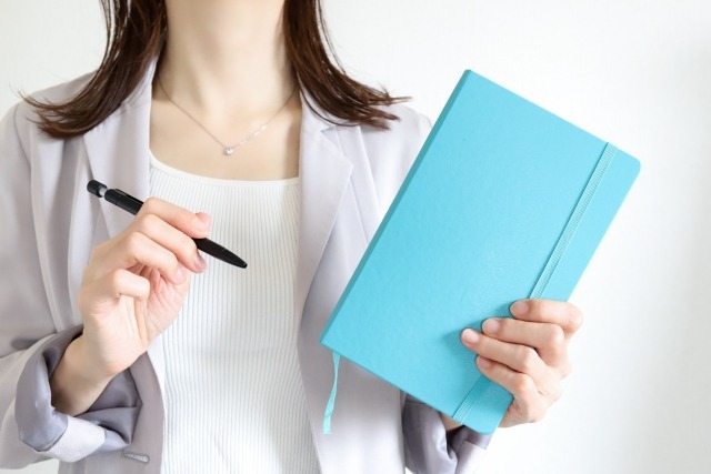 画像：右手にペン、左手にノートを持つ女性の写真