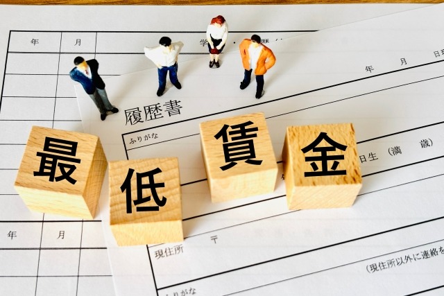 画像:履歴書の上に「最低賃金」と書かれた木製ブロックが置かれている