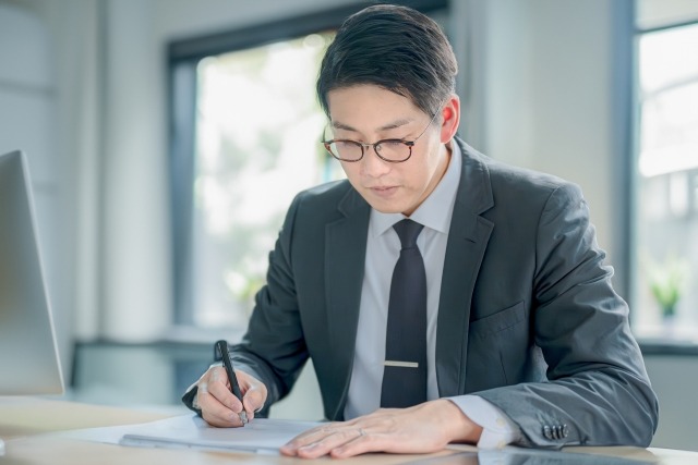 画像:スーツを着たビジネスマンが机に向かいメモを取っている写真