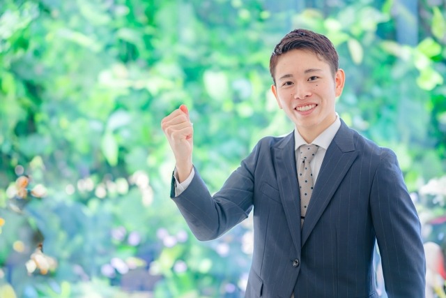 画像:スーツを着た男性が自然を背景にガッツポーズをしている写真