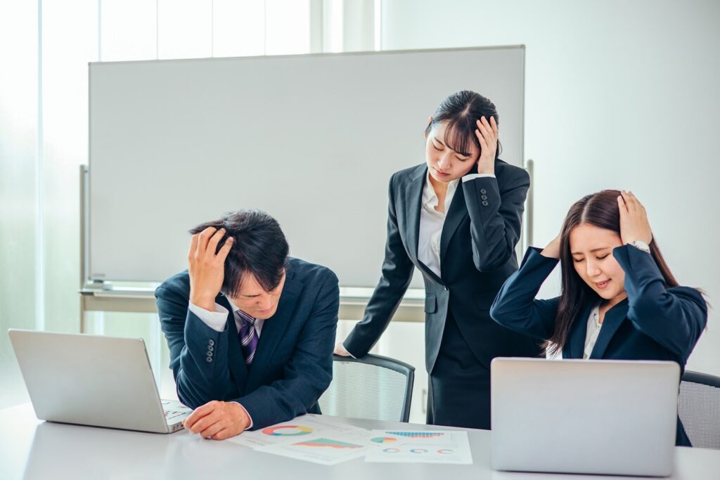 画像：男女3人のビジネスパーソンがオフィスで頭を抱えている写真