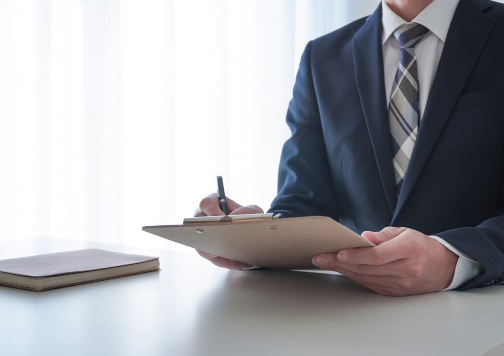 画像：男性のビジネスパーソンがペンとクリップボードをもっている写真