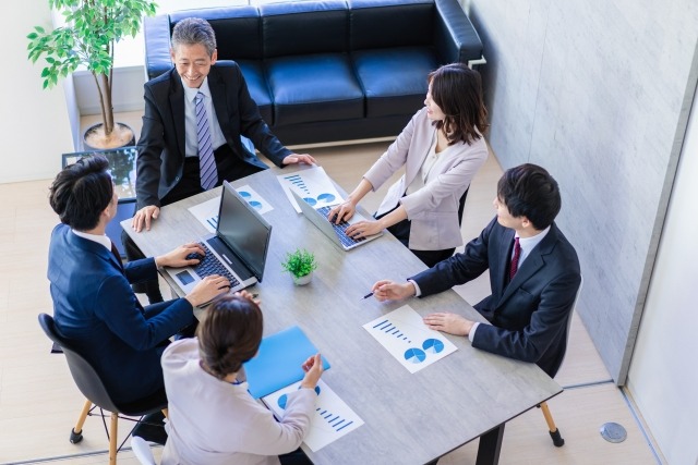 画像：５人のビジネスパーソンが机を挟み談笑している写真