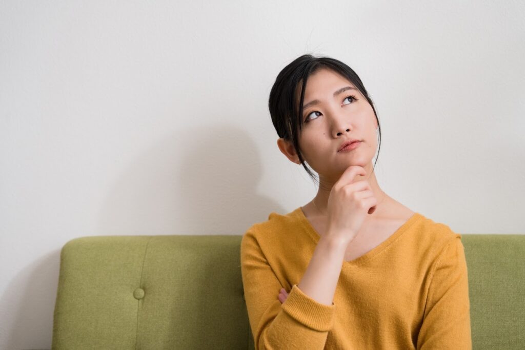 画像:女性が椅子に座り、左斜め上を見て首をかしげている写真