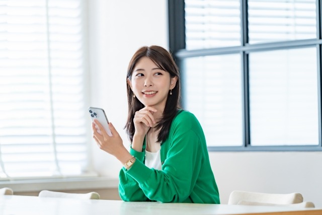 画像：スマートフォンを片手に微笑む女性の写真